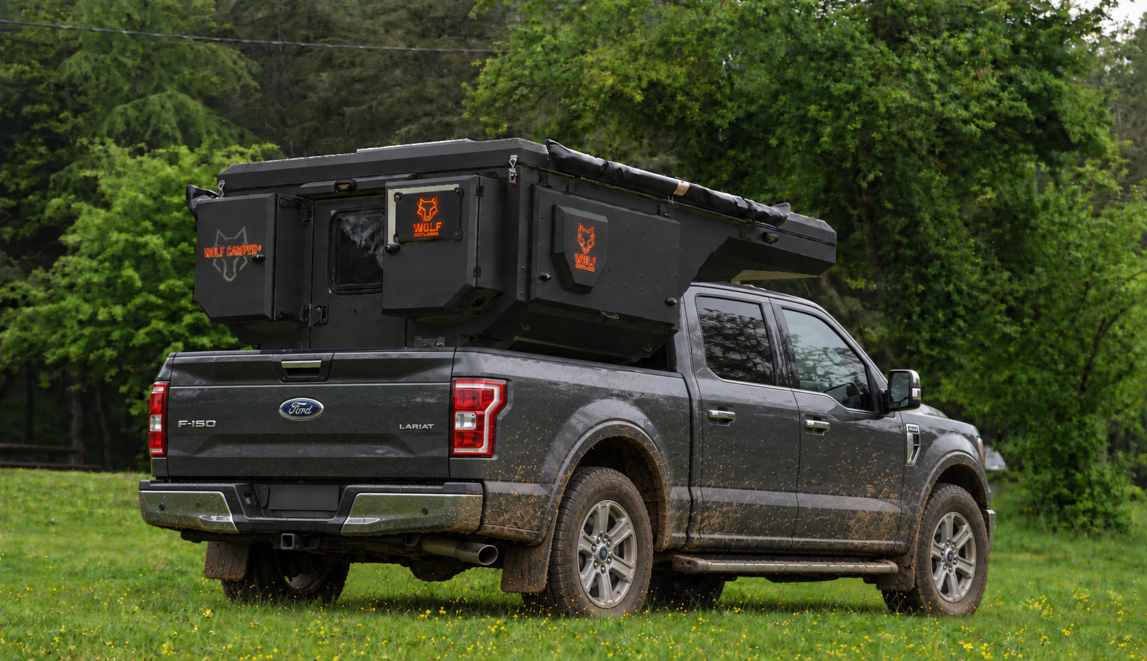 Rear three-quarter view of a grey Ford F-150 Lariat with a matt black WOLF CAMPER pickup camper and orange WOLF signatures in the forest.