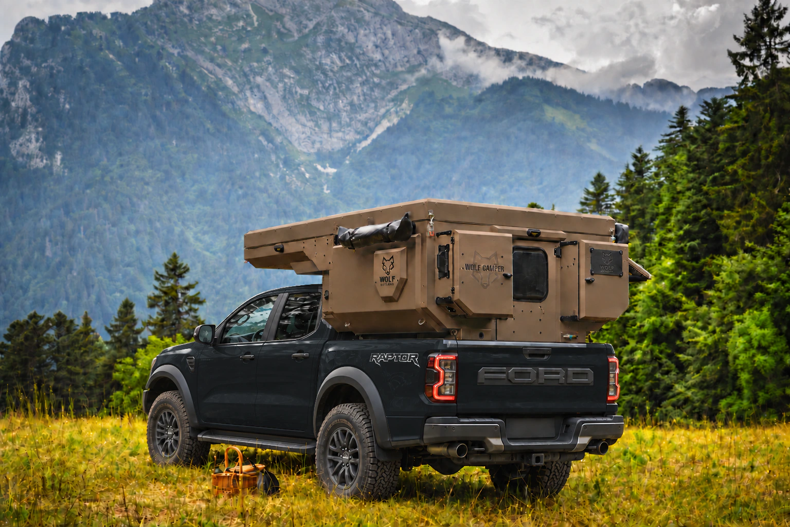 Rear three-quarter view of a black Ford Ranger Raptor with a desert sand WOLF CAMPER in a mountain meadow.