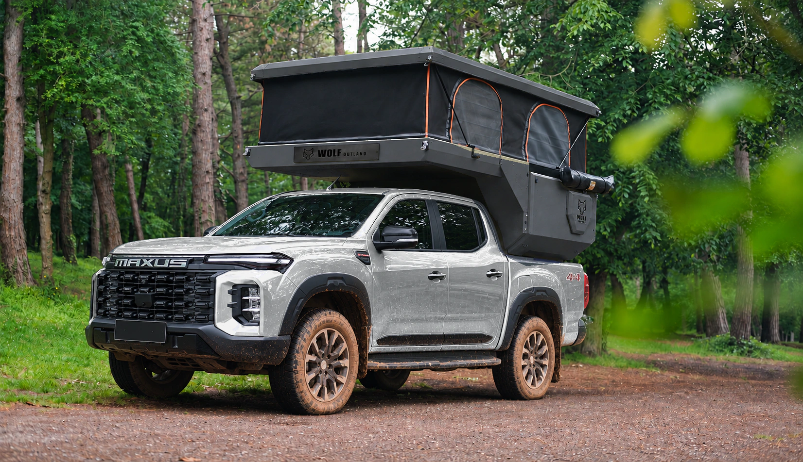 Front three-quarter view of a silver MAXUS T60 MAX with a graphite WOLF CAMPER pickup camper and raised roof in the forest.