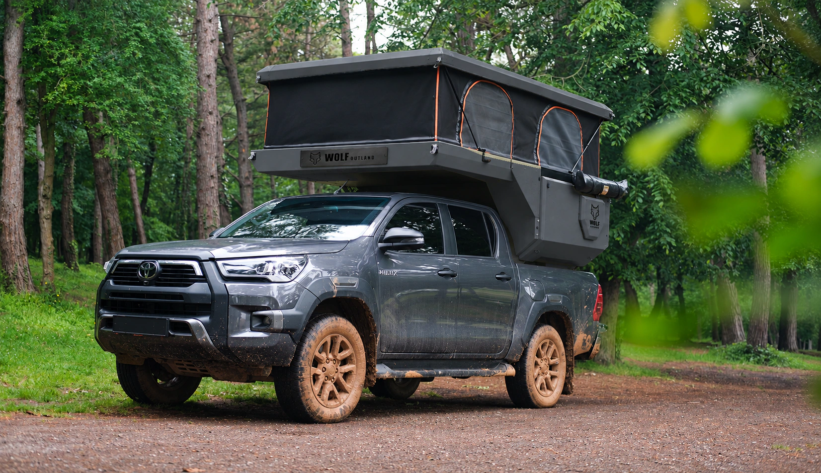 Toyota Hilux in anthracite grey with WOLF CAMPER in Graphite, solid cabinets — Front left three-quarter, Roof raised, Black laser engraving.