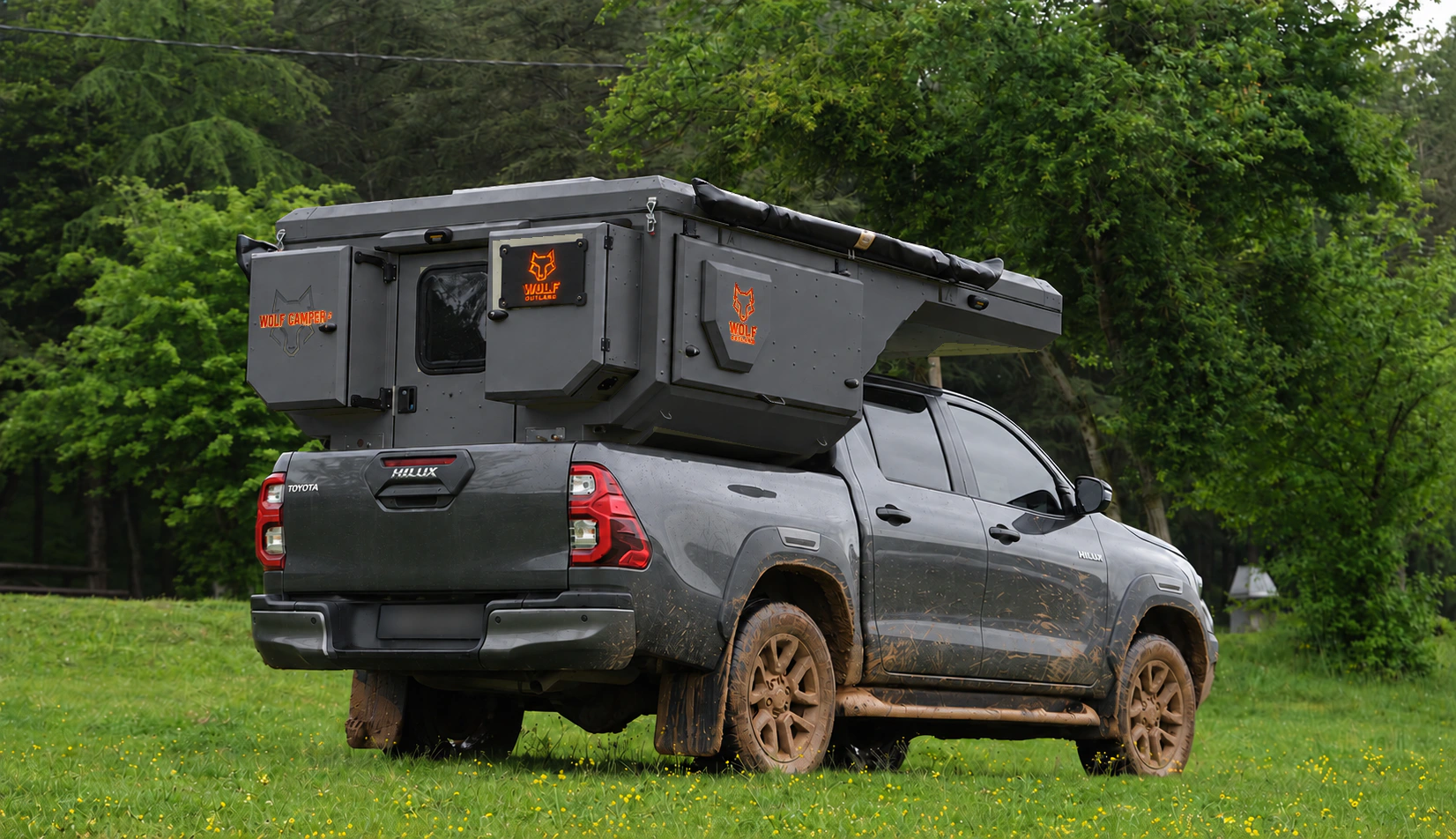 Toyota Hilux in anthracite grey with WOLF CAMPER in Graphite, solid cabinets — Rear right three-quarter, Roof closed, Orange backlighting.