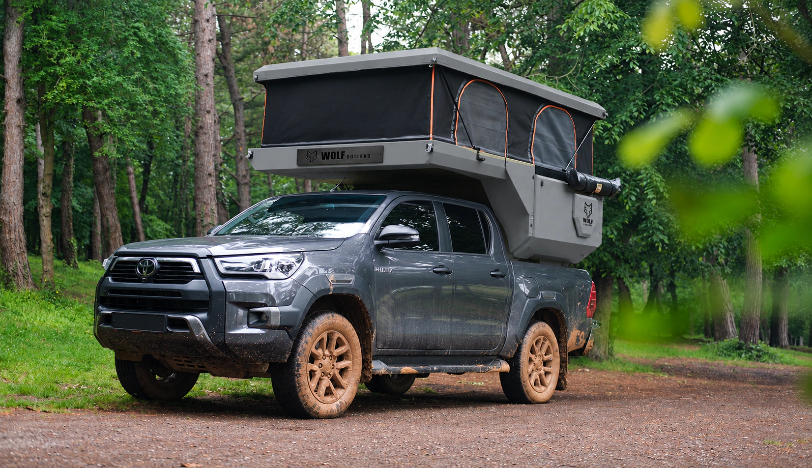 Toyota Hilux in anthracite grey with WOLF CAMPER in Mineral grey, solid cabinets — Front left three-quarter, Roof raised, Black laser engraving.