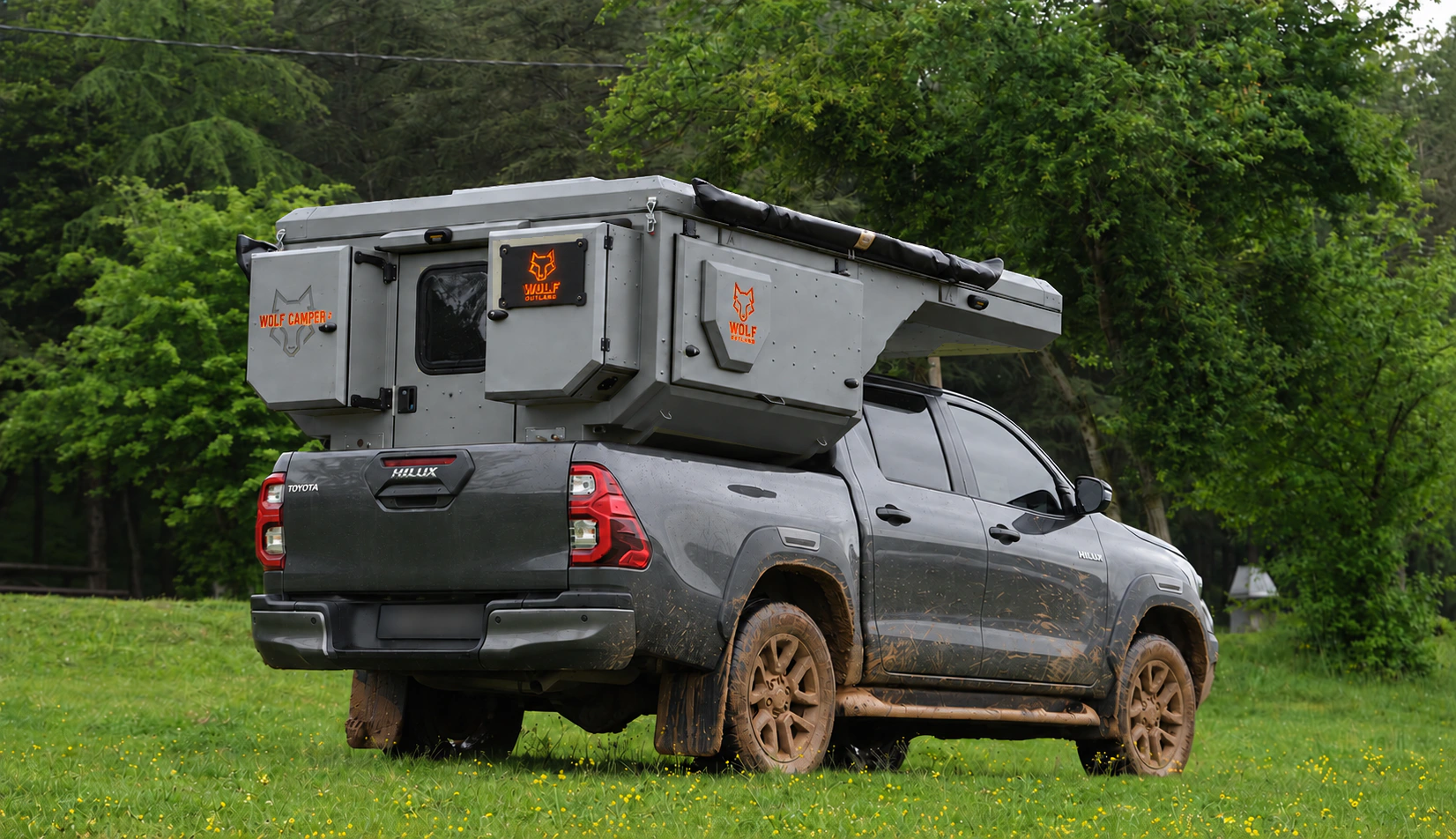 Toyota Hilux in anthracite grey with WOLF CAMPER in Mineral grey, solid cabinets — Rear right three-quarter, Roof closed, Orange backlighting.