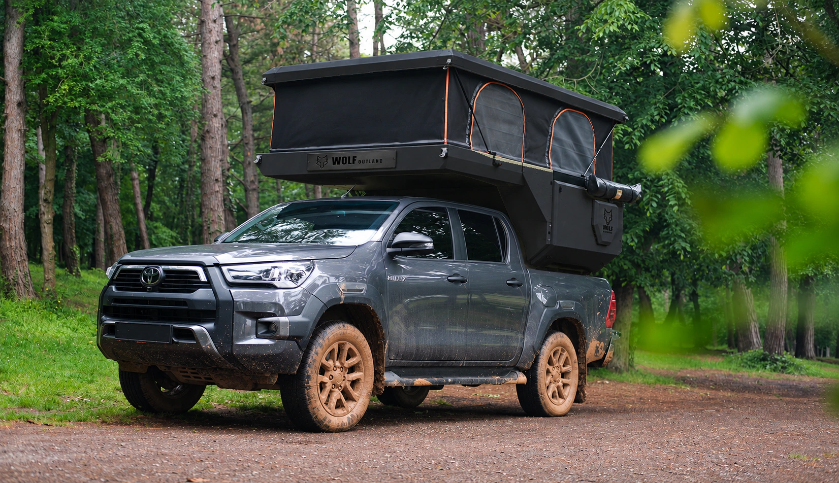 Toyota Hilux in anthracite grey with WOLF CAMPER in Matt black, solid cabinets — Front left three-quarter, Roof raised, Black laser engraving.