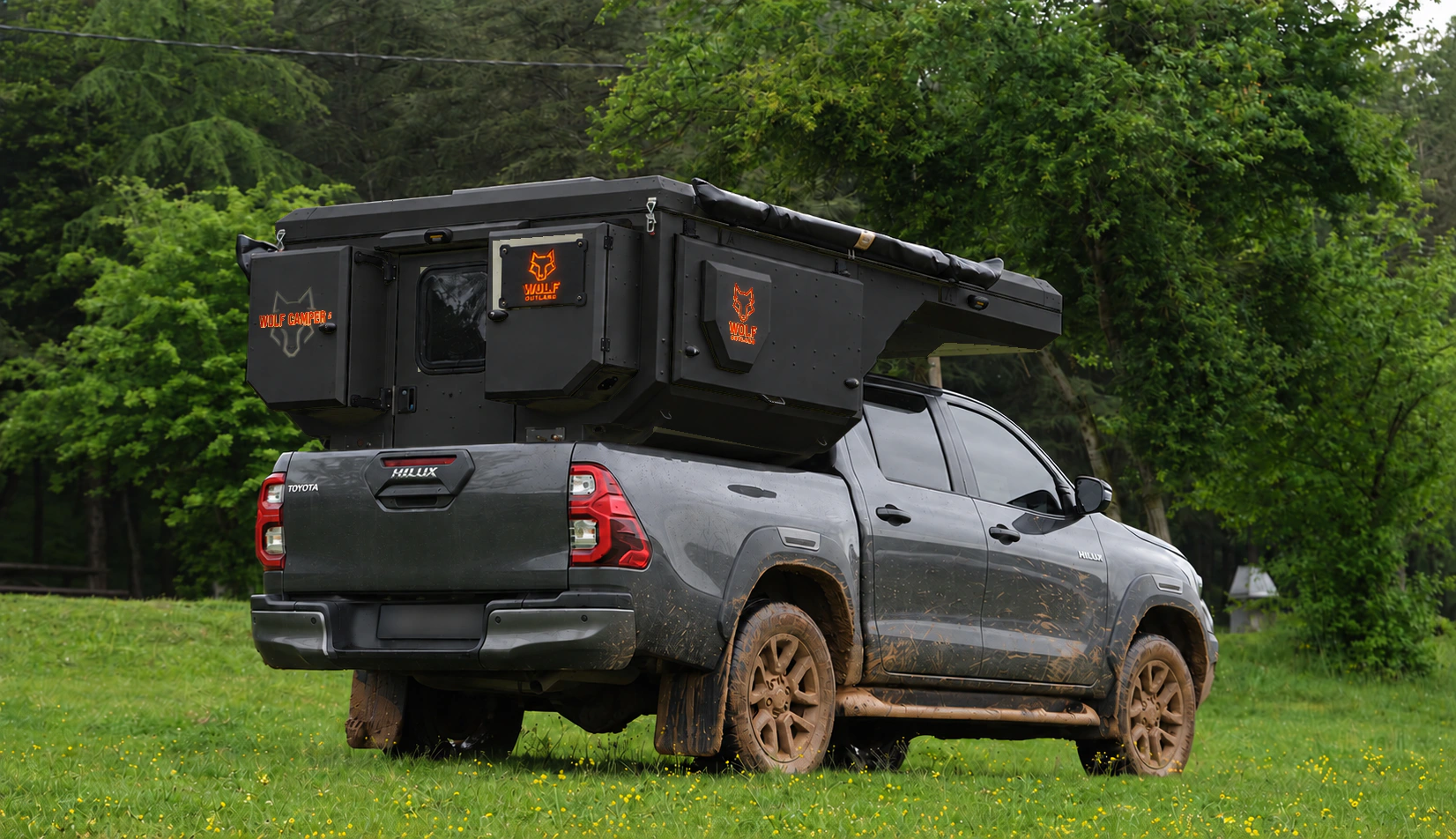Toyota Hilux in anthracite grey with WOLF CAMPER in Matt black, solid cabinets — Rear right three-quarter, Roof closed, Orange backlighting.
