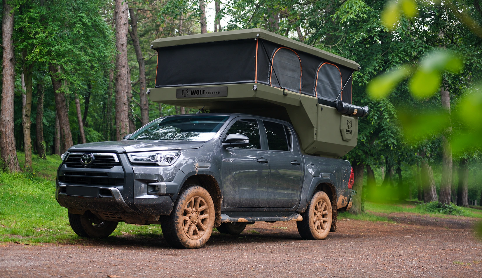 Toyota Hilux in anthracite grey with WOLF CAMPER in Tactical olive, solid cabinets — Front left three-quarter, Roof raised, Black laser engraving.