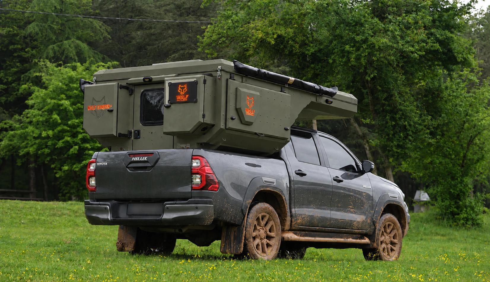 Toyota Hilux in anthracite grey with WOLF CAMPER in Tactical olive, solid cabinets — Rear right three-quarter, Roof closed, Orange backlighting.