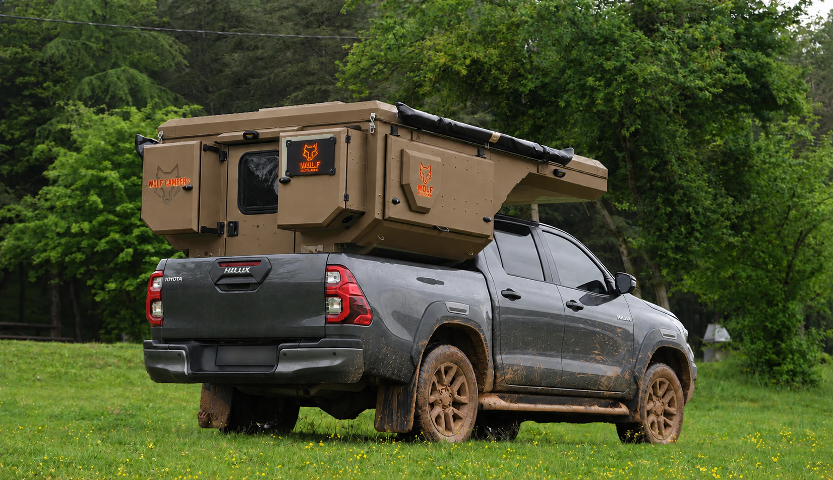 Toyota Hilux in anthracite grey with WOLF CAMPER in Bronze, solid cabinets — Rear right three-quarter, Roof closed, Orange backlighting.