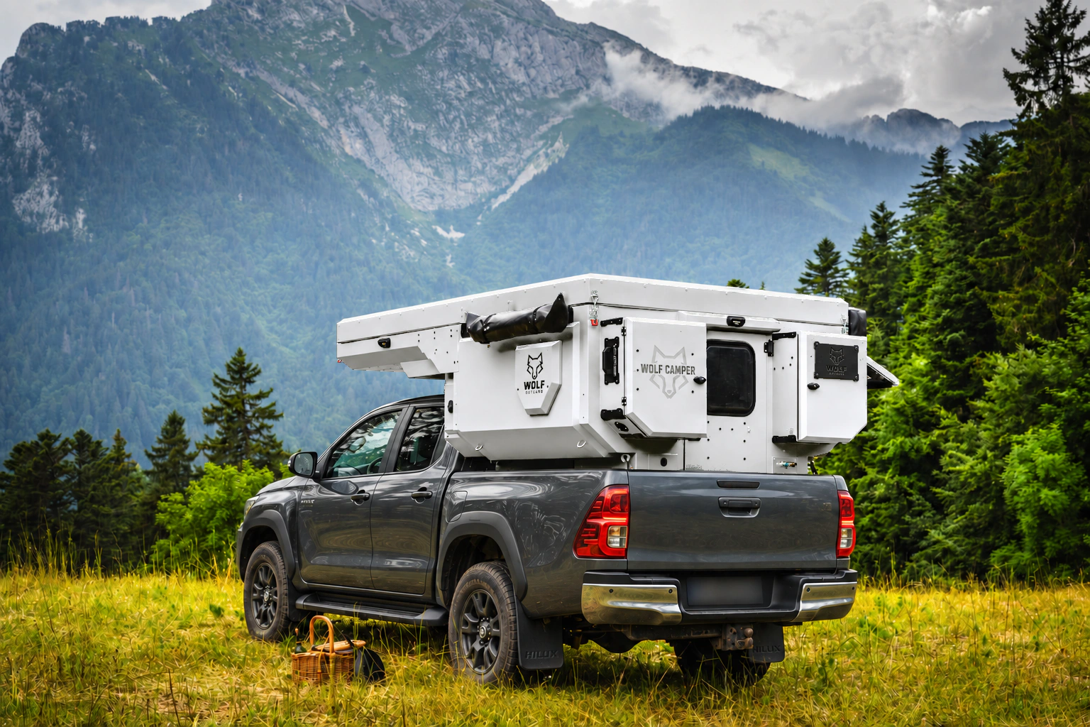 Toyota Hilux in anthracite grey with WOLF CAMPER in Glacier white, solid cabinets — Rear left three-quarter, Roof closed, Black laser engraving.