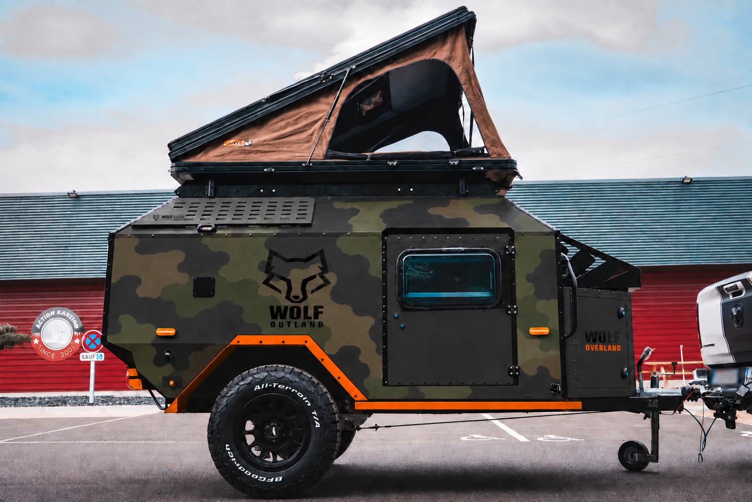 Side view of WOLF Overland caravan in army camouflage, tent raised · doors closed. Side view of WOLF Overland caravan in army camouflage, tent raised · doors closed.