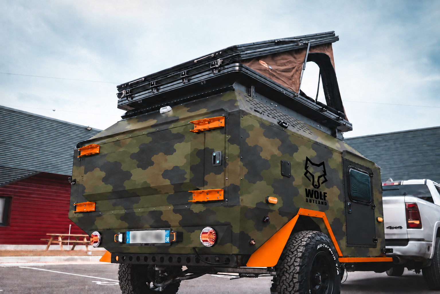 Rear three-quarter view of WOLF Overland caravan in army camouflage, tent raised · storage closed.