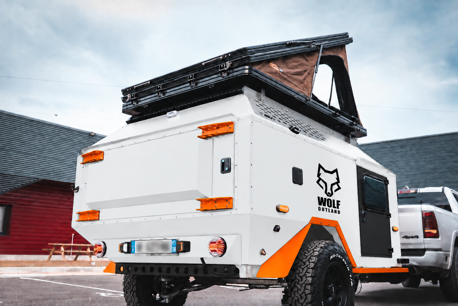 Rear three-quarter view of WOLF Overland caravan in glacier white, tent raised · storage closed.