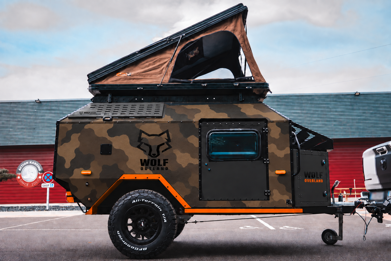Side view of WOLF Overland caravan in dark desert camouflage, tent raised · doors closed.