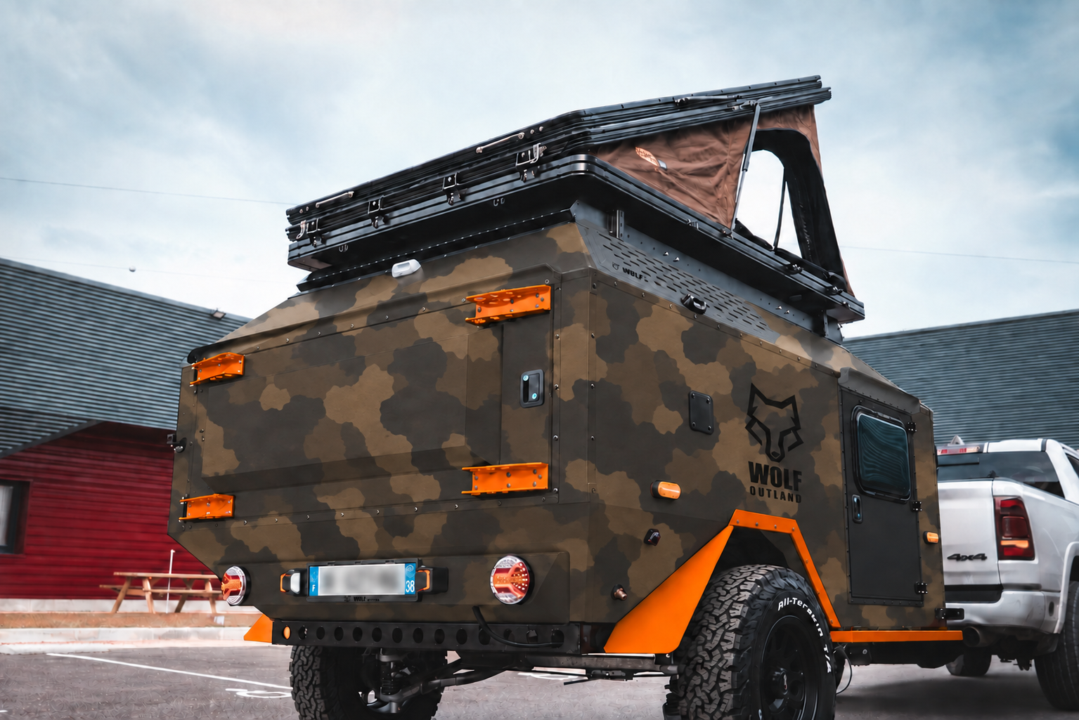 Rear three-quarter view of WOLF Overland caravan in dark desert camouflage, tent raised · storage closed.