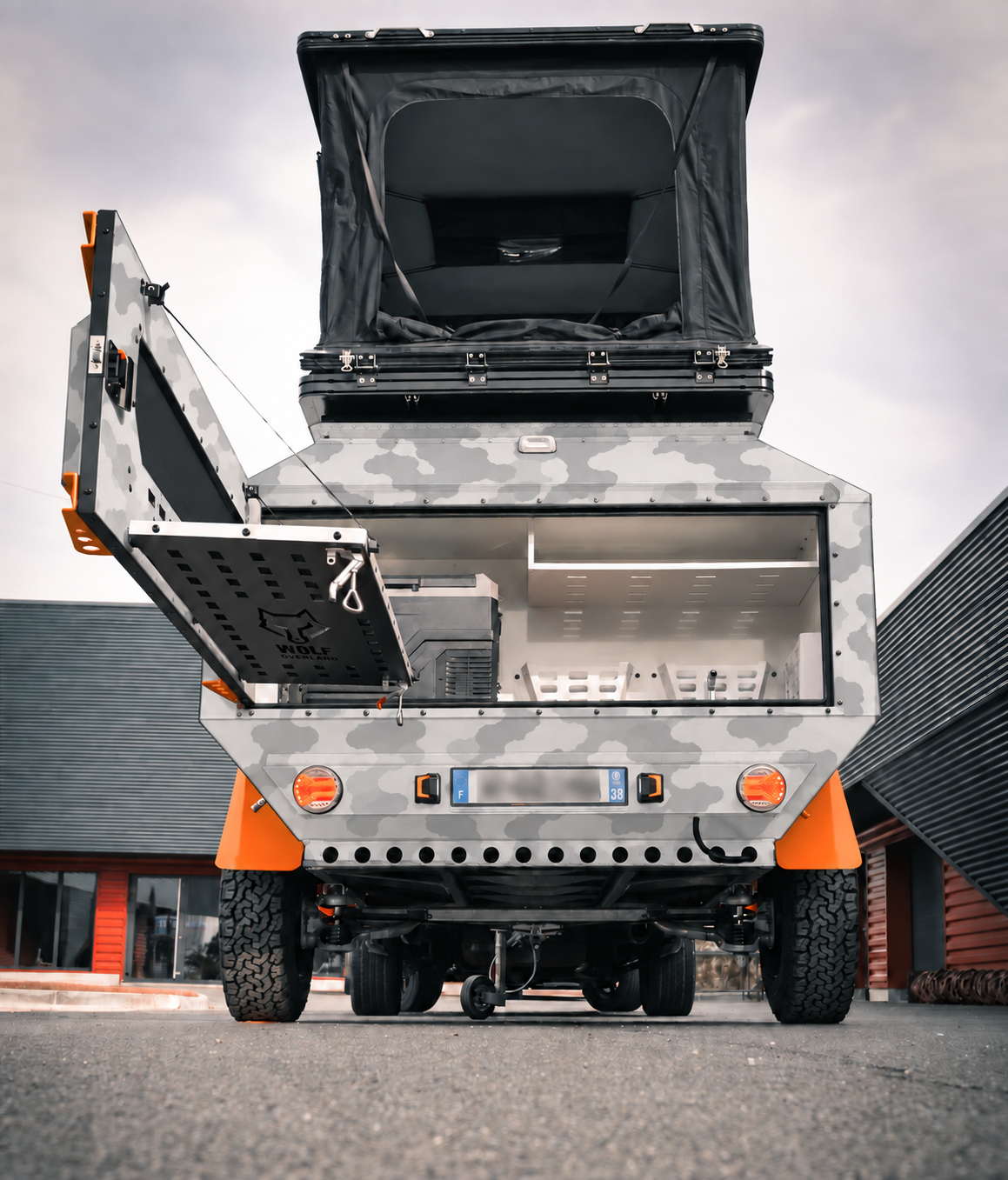 Rear view of WOLF Overland caravan in light snow camouflage, tent raised · storage open.