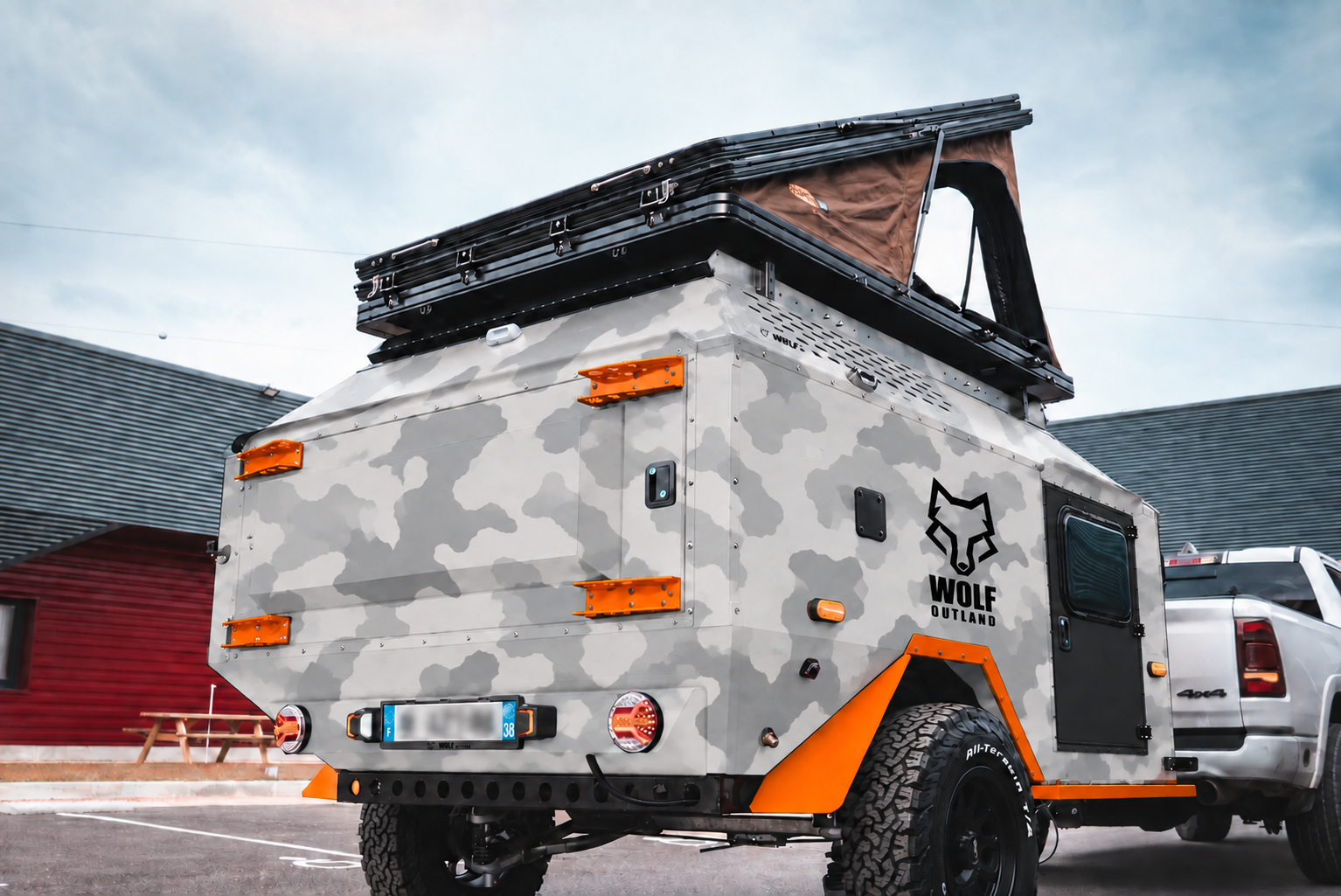 Rear three-quarter view of WOLF Overland caravan in light snow camouflage, tent raised · storage closed.