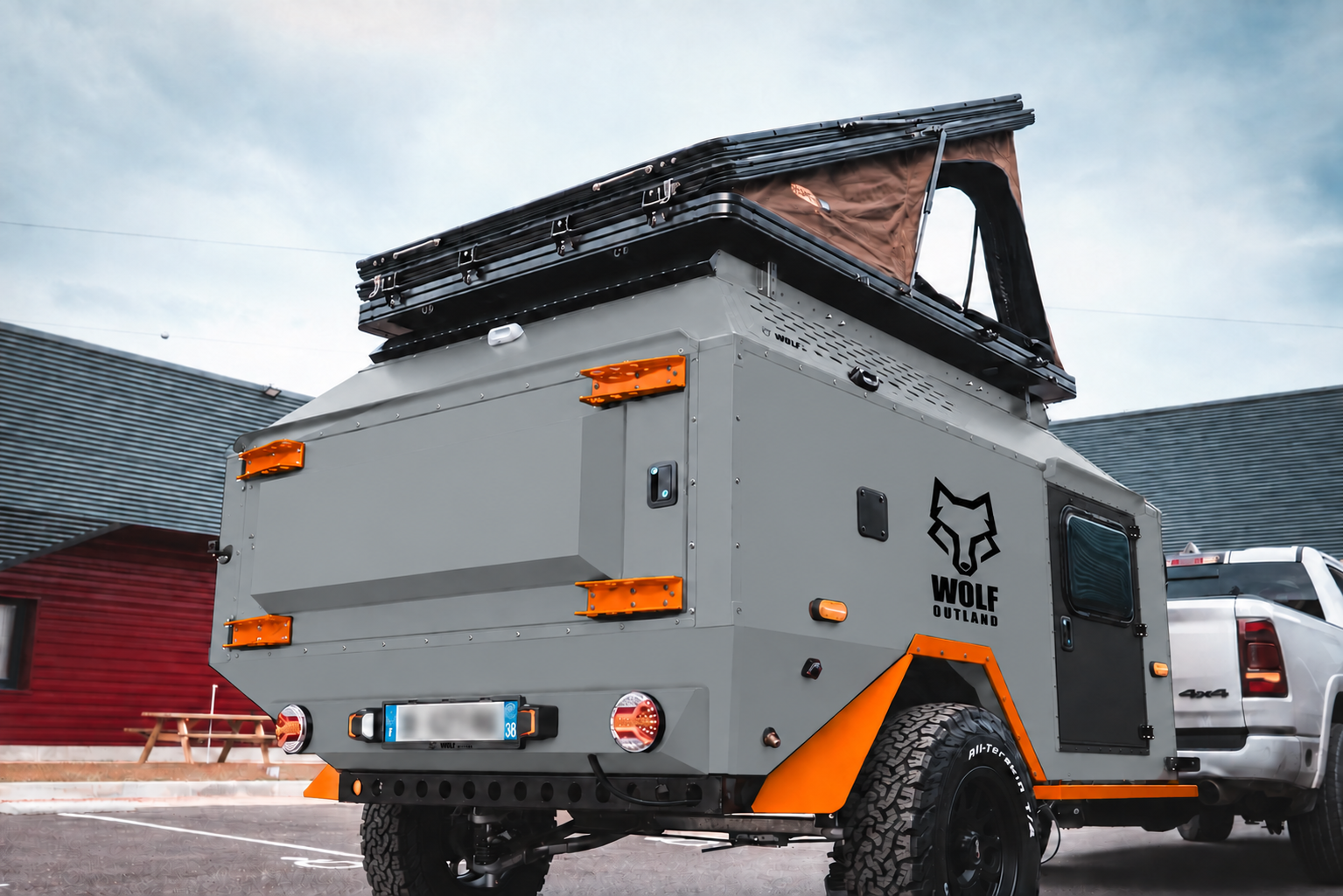 Rear three-quarter view of WOLF Overland caravan in mineral grey, tent raised · storage closed.