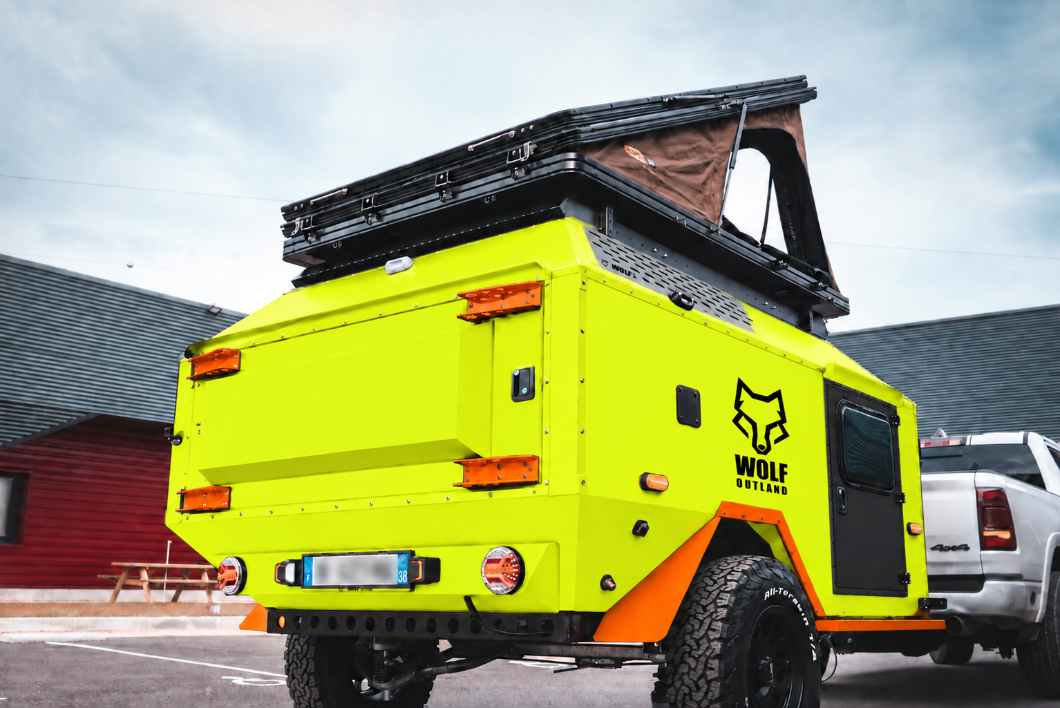 Rear three-quarter view of WOLF Overland caravan in fluorescent yellow, tent raised · storage closed.