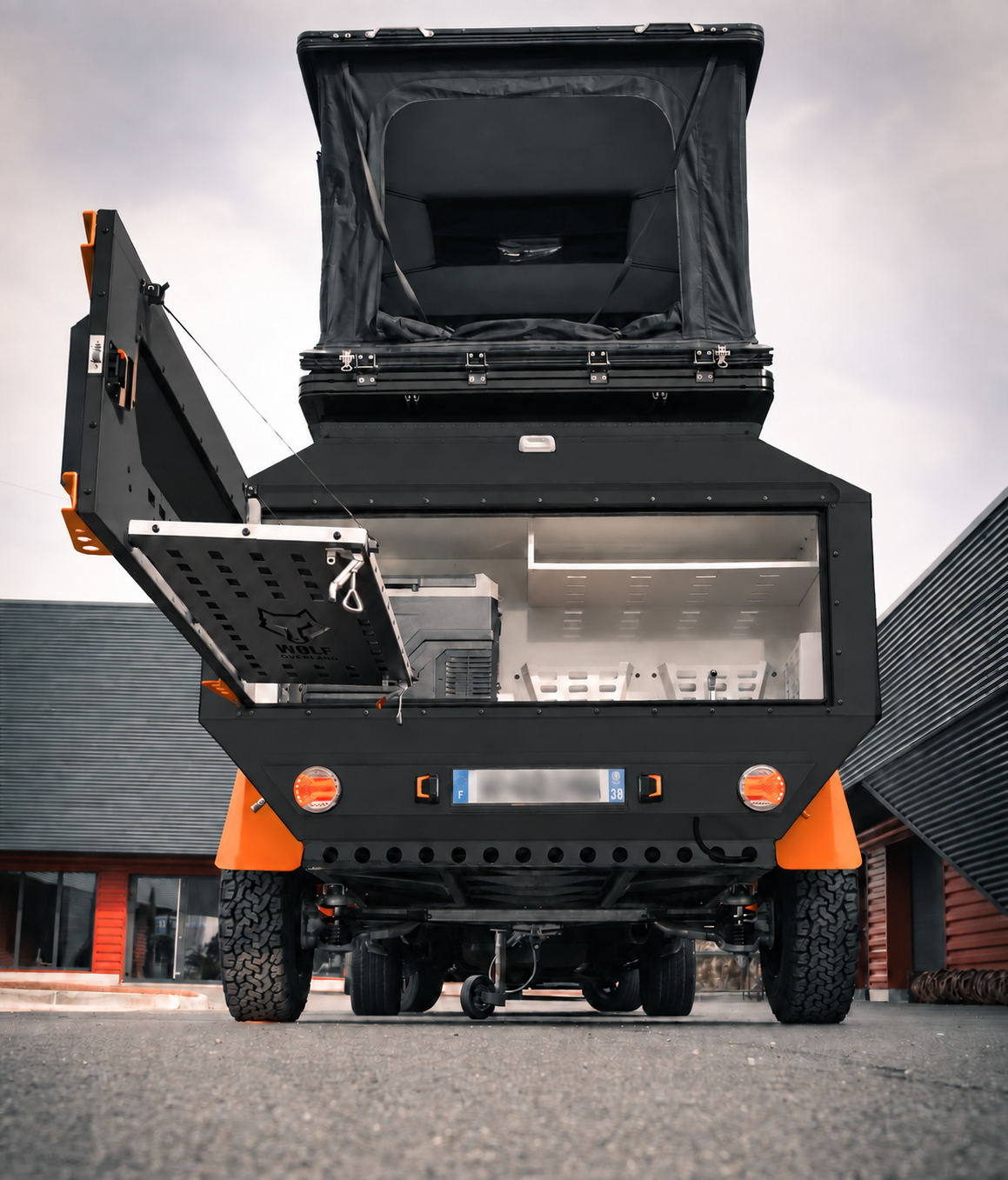Rear view of WOLF Overland caravan in matt black, tent raised · storage open.