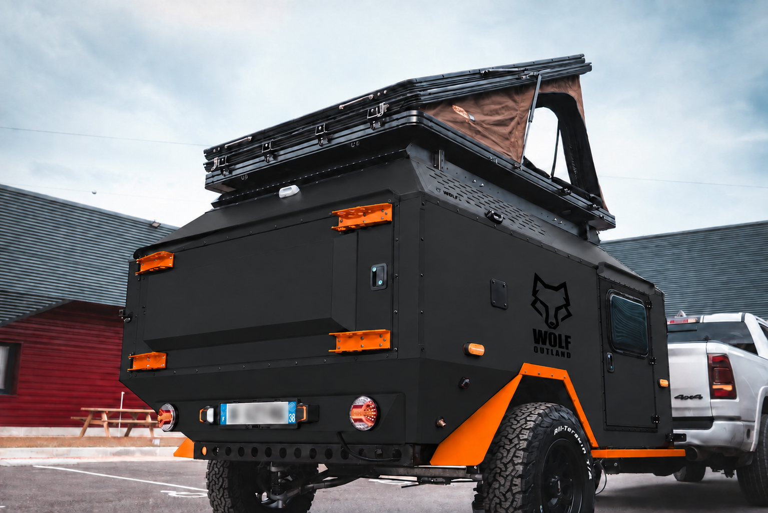 Rear three-quarter view of WOLF Overland caravan in matt black, tent raised · storage closed.