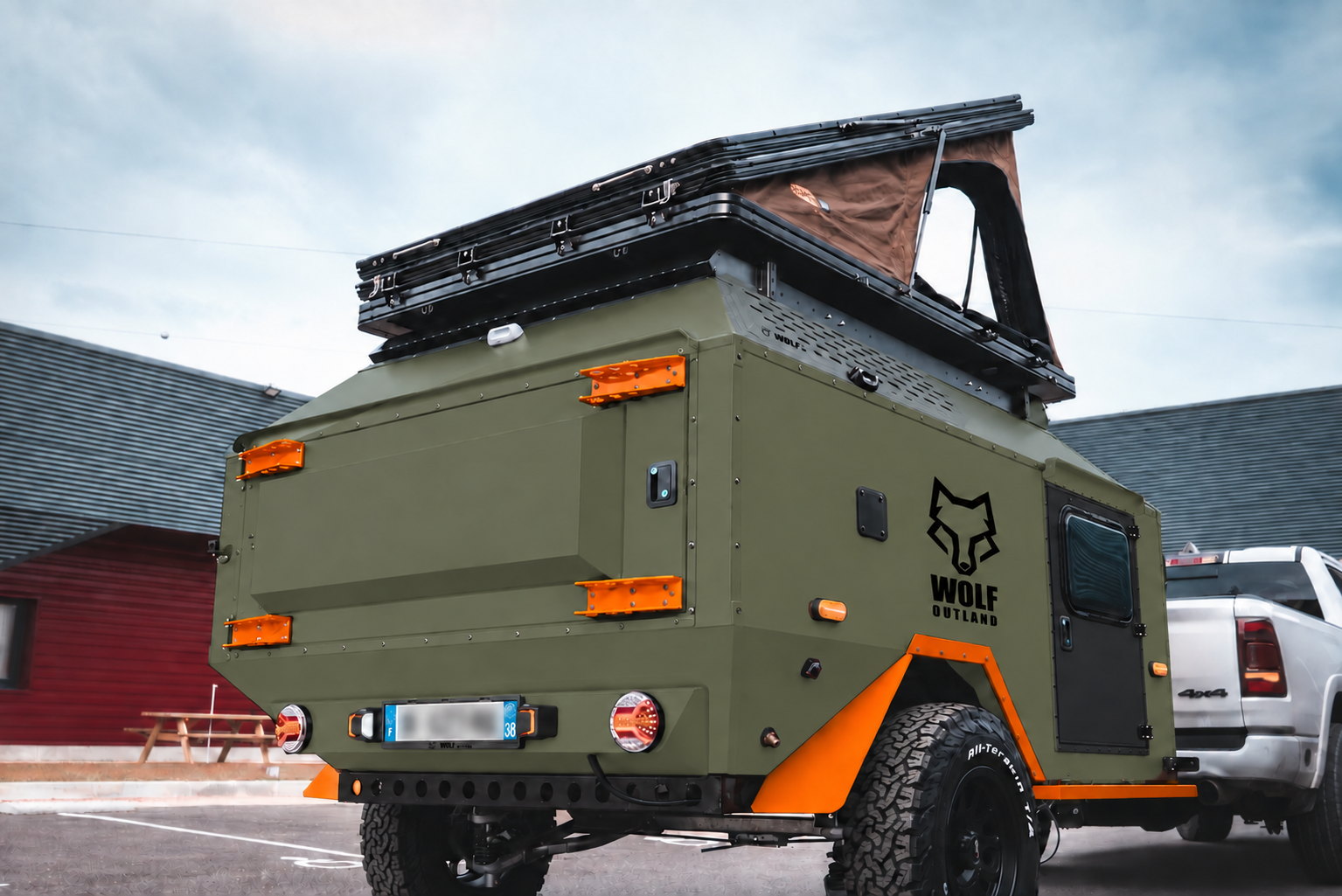 Rear three-quarter view of WOLF Overland caravan in tactical olive, tent raised · storage closed.