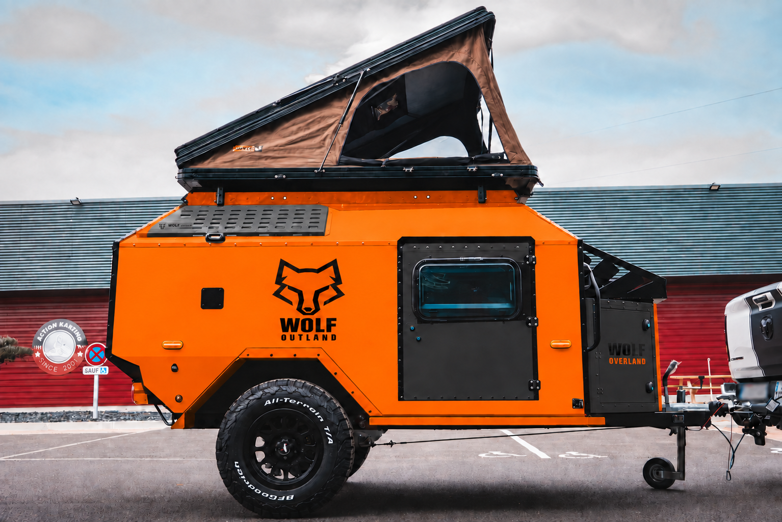 Side view of WOLF Overland caravan in fluorescent orange, tent raised · doors closed.