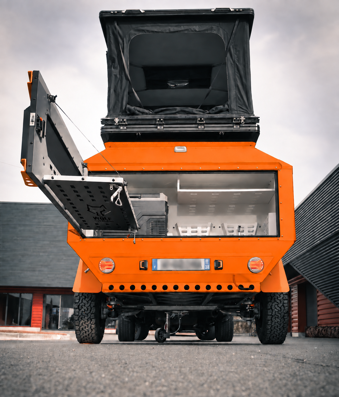 Rear view of WOLF Overland caravan in fluorescent orange, tent raised · storage open.