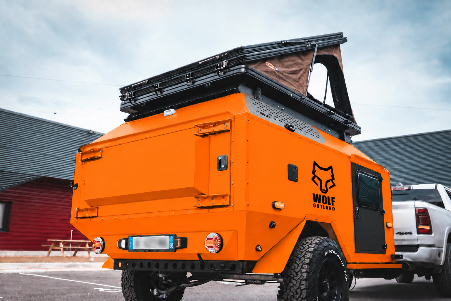 Rear three-quarter view of WOLF Overland caravan in fluorescent orange, tent raised · storage closed.