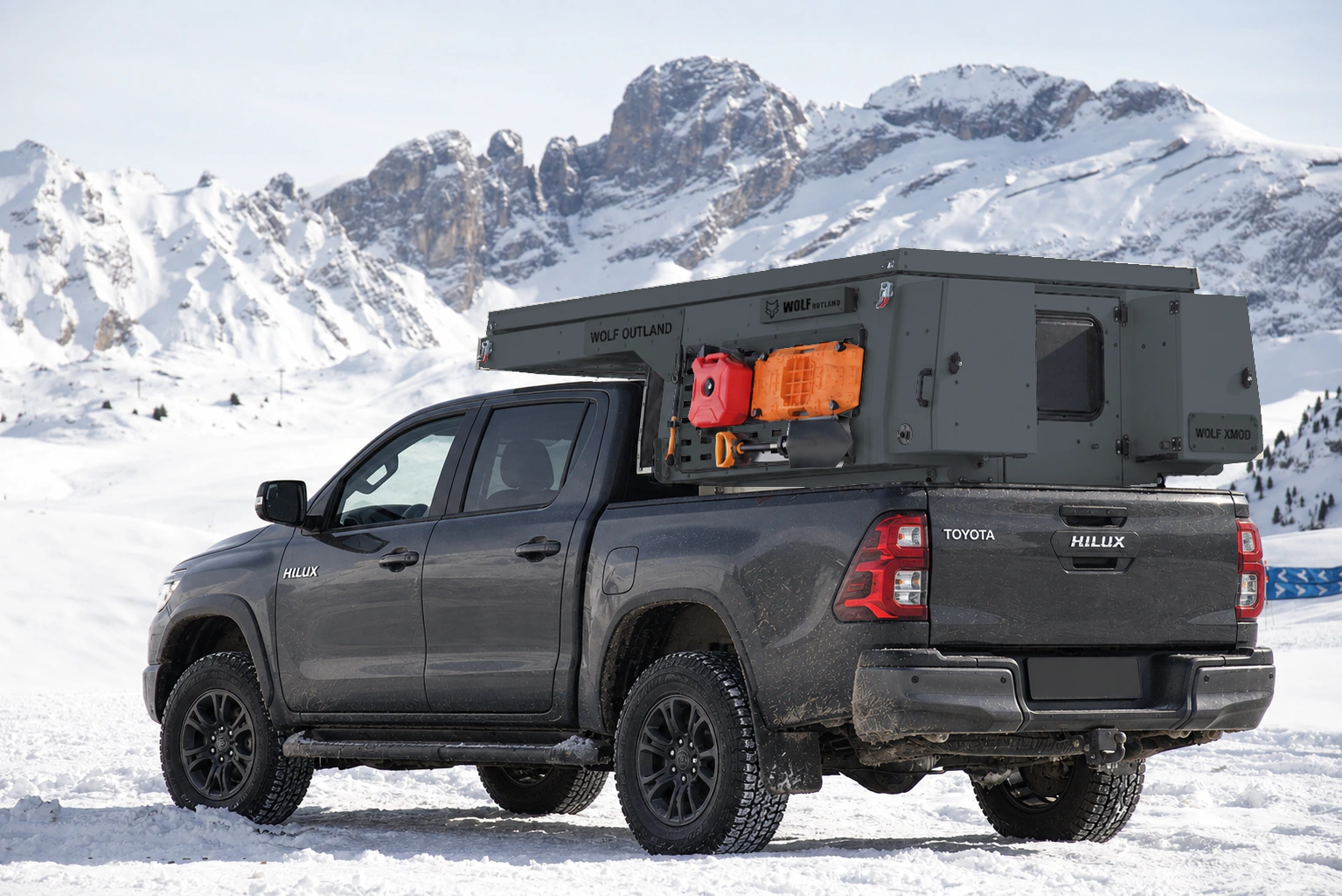 Toyota Hilux in anthracite grey with WOLF XMOD in Graphite, two solid rear cabinets — Rear left three-quarter view, roof closed, Black engravings.