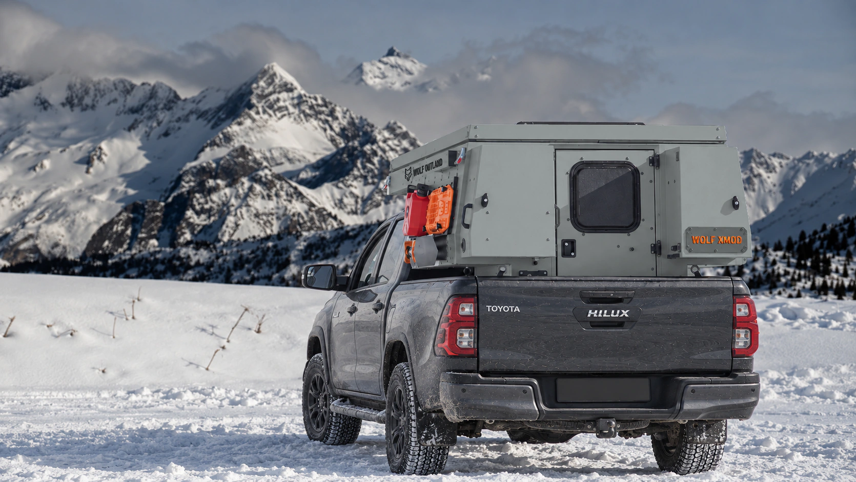 Toyota Hilux in anthracite grey with WOLF XMOD in Mineral grey, two solid rear cabinets — Rear view, roof closed, Orange backlit WOLF XMOD plate.