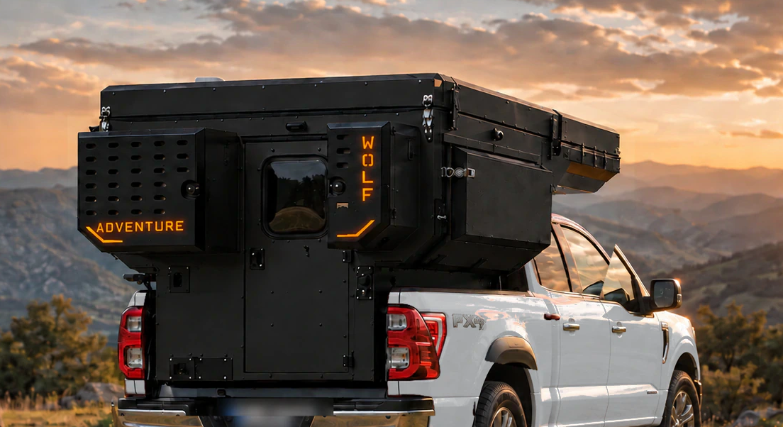 Rear close-up of a matt black WOLF ADVENTURE pickup camper on a silver Ford F-150, with a perforated storage box and orange markings.