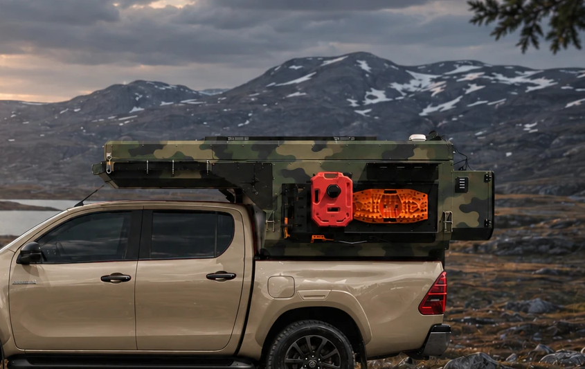 Side close-up of the orange and red equipment on a WOLF ADVENTURE Army camouflage pickup camper mounted on a sand Toyota Hilux.